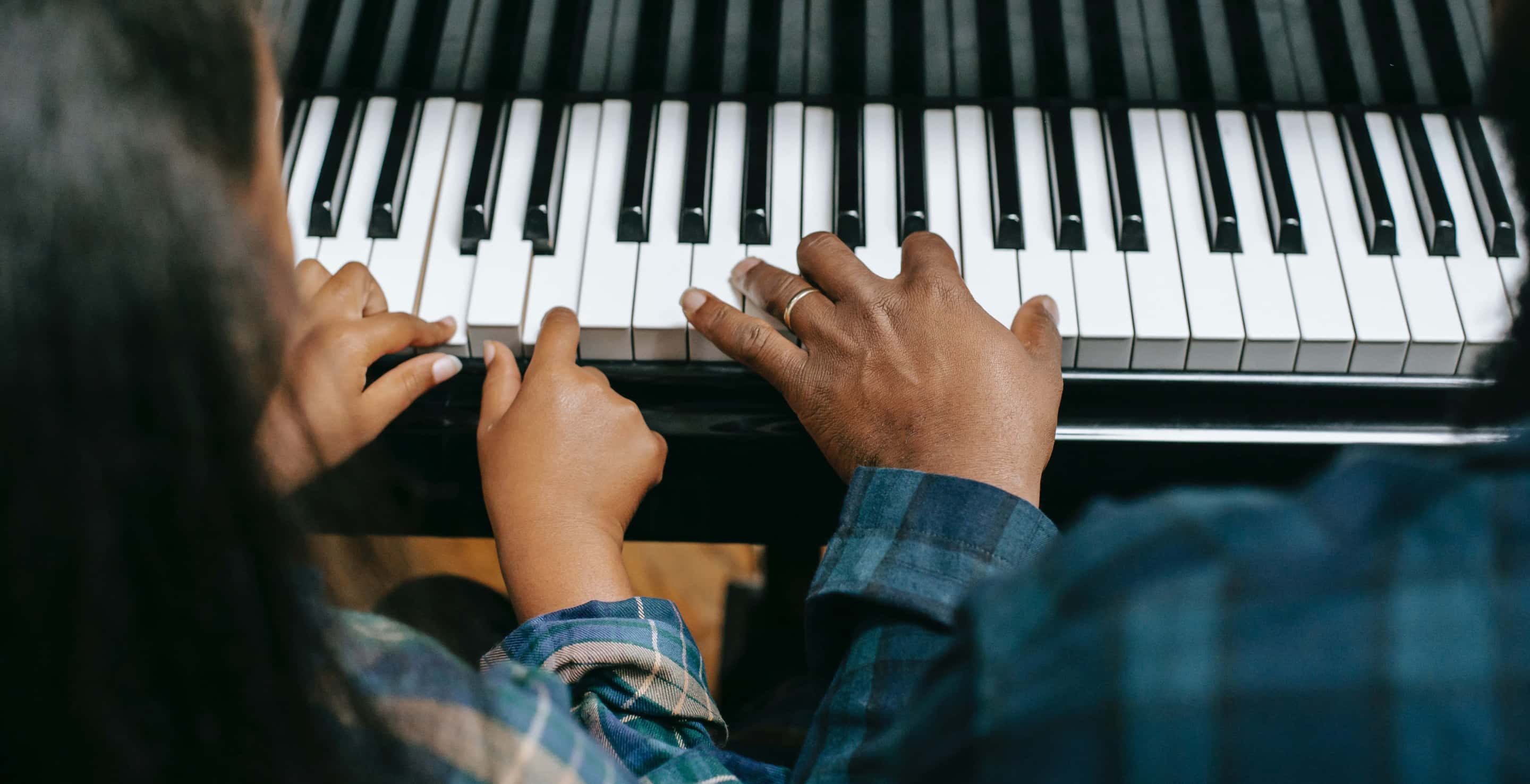 Eine Erwachsenenhand neben zwei Kinderhänden am Klavier