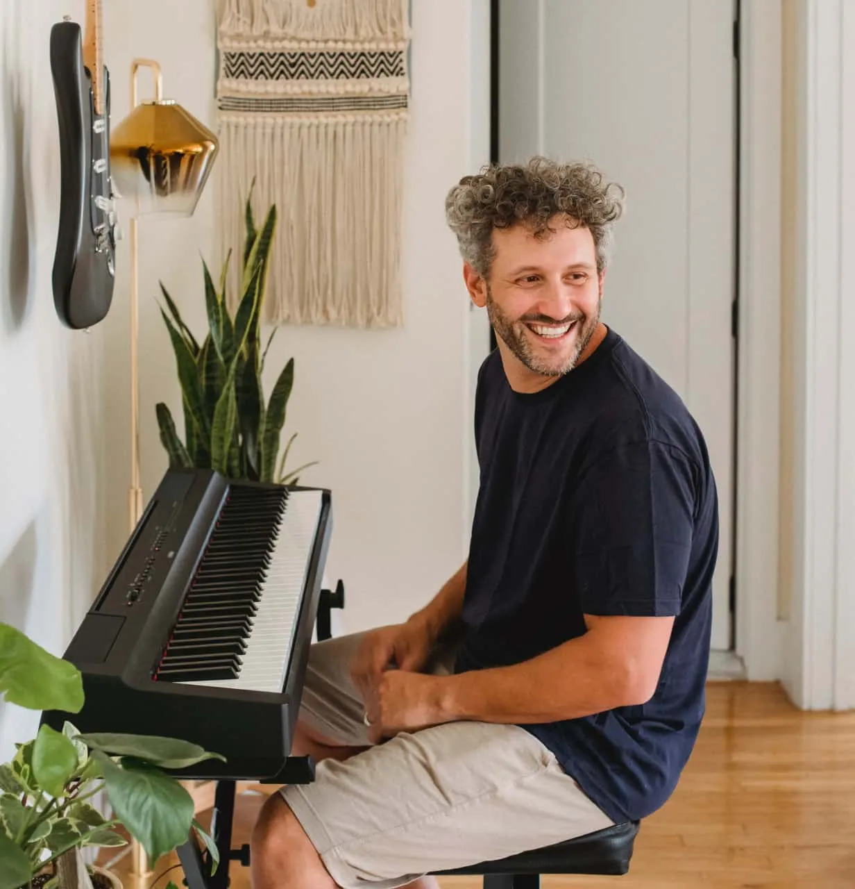 Mann sitzt an E-Piano und guckt lachend über seine Schulter